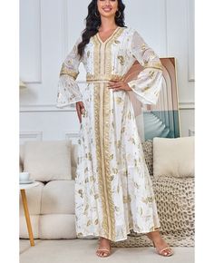 a woman standing in front of a couch wearing a white and gold dress