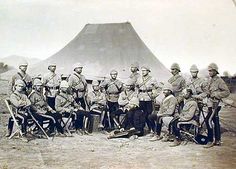 a group of men in uniforms standing next to each other on a dirt field with a mountain in the background