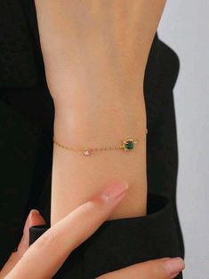 a woman wearing a gold bracelet with an emerald stone on the side and a small diamond in the middle