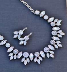 "A stunning new necklace made entirely using Swarovski crystals and elements. The necklace is a cluster style, with various shaped and sizes of stones. There are larger marquise clusters, underneath embellished flower links, each set with teeny crystals. Stones range in color from crystal clear, crystal moonlight, white opal, white pearl, and more. Each stone is painstakingly set by hand, and either prong or pave set. Jeweled portion of the necklace measures 8\" wide, and connects to rhodium pla Dazzling White Bridal Necklace With Sparkling Stones, White Crystal Embellished Jewelry For Anniversary, Formal White Bridal Necklace With Rhinestones, Formal White Rhinestone Bridal Necklace, White Crystal Rhinestone Necklace For Wedding, Dazzling White Rhinestone Necklace For Wedding, Dazzling White Rhinestone Bridal Necklace, Dazzling White Bridal Necklace With Rhinestones, Sparkling White Rhinestone Necklace For Wedding