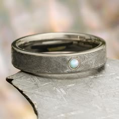 a wedding band with a white opal in the center on top of a piece of metal