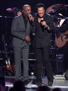 two men singing on stage with one holding a microphone and the other wearing a suit