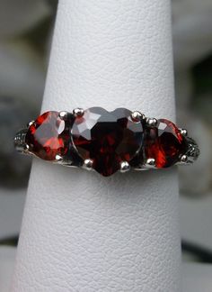 "Red Garnet Cubic Zirconia Ring Description Hearts Design#143 Made To Order This is a lovely Edwardian inspired ring in solid sterling silver. The gorgeous filigree ring is set with 3 heart cut simulated/Man-made garnet red CZ gemstones. The 2 smaller gems are 5mm in diameter, and the center one is 7mm in diameter. Notice the amazing etched band... The ring sits 1/4th\" (7mm) off the finger. The quality of the silver and gemstones are simply breathtaking... a ring that will last for countless ye Heart Shaped Red Ruby Ring For Wedding, Heart-shaped Red Ruby Wedding Ring, Red Heart Cut Rings For Wedding, Elegant Multi-stone Jewelry For Valentine's Day, Red Heart-shaped Birthstone Jewelry, Red Heart Shaped Wedding Rings, Red Sterling Silver Gemstones For Anniversary, Red Garnet Round Cut Jewelry, Fine Jewelry Red Heart Ring For Wedding