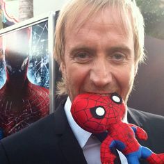 a man in a suit and tie holding a stuffed spiderman toy to his mouth