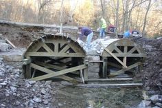 two men are working on the construction of a bridge over a stream in the woods