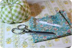 scissors and fabric on a table next to a green flowered pillow with an apple in the background