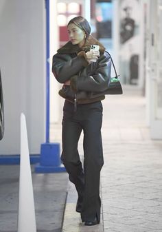 a woman is walking down the sidewalk with her hand in her pocket and holding a coffee cup