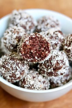 a bowl filled with chocolate covered donuts on top of a wooden table