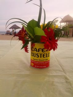 a can with flowers in it sitting on a table next to the beach and umbrellas