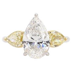 a yellow and white diamond ring with three pear shaped diamonds on the sides, set in 18k gold