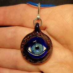 "Eyes have always been a fascination of mine. I make each handmade eye pendant using a blowtorch and Borosilicate glass in my studio. Some people refer to these eye pendants as Evil Eye Pendants. The evil eye has always been an ancient symbol that brings protection and good luck from any negative energy. I just like making eyes that look realistic, and glow from the silver in the glass. A lot goes into making these Evil Eye Pendants. First, I must create a murrini cane with the pupil and iris. I Handmade Teardrop Glass Jewelry, Murano Glass Pendant Necklace For Gift, Handmade Round Necklace With Eco-friendly Glass, Handmade Round Recycled Glass Necklace, Unique Evil Eye Necklace For Gift, Spiritual Clear Glass Necklaces, Round Recycled Glass Necklaces For Gifts, Murano Glass Round Necklace For Gifts, Murano Glass Round Necklaces For Gifts