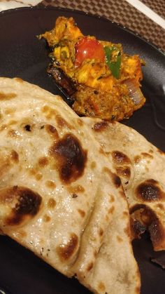 two flat breads on a black plate next to a side dish