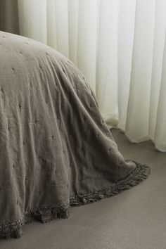 an unmade bed in front of a window with white curtains