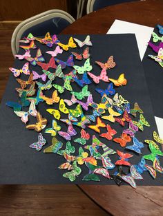 a table topped with lots of colorful paper butterflies on top of a piece of black paper