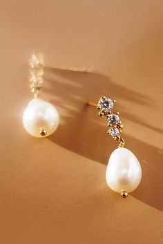 two pearl and diamond earrings sitting on top of a brown surface with the shadow of a person's head