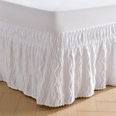 a white bed skirt with ruffles on the top and bottom, sitting on a wooden floor