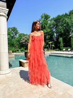 a woman standing in front of a pool wearing an orange dress