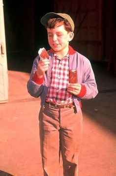 a young boy is holding something in one hand and wearing a hat on the other