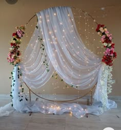 a white drape with flowers and lights hanging from it's sides on the floor