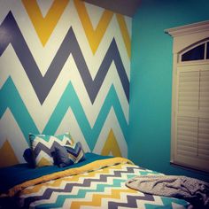 a bed sitting under a window next to a wall painted with colorful chevrons