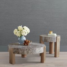 two marble tables with flowers on them in front of a gray wall and wooden floor