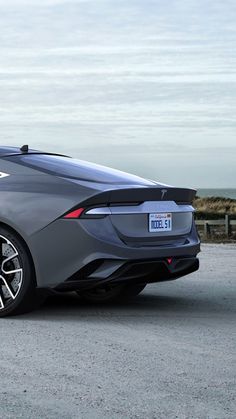 a grey sports car parked on the side of a road next to a fence and ocean