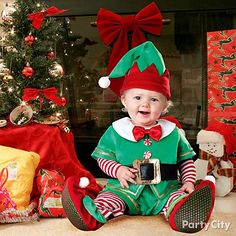 a baby dressed in elf costume sitting next to christmas presents