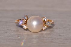 a pearl and diamond ring sitting on top of a wooden table