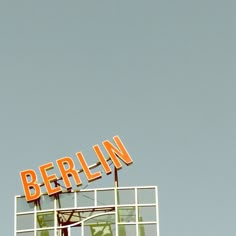 an orange berlin sign on top of a glass building with the sky in the background