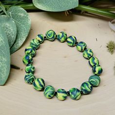 a green and blue beaded bracelet sitting on top of a wooden table next to plants