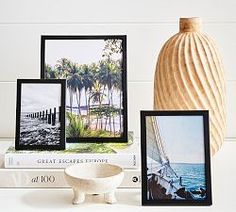 there are three pictures on the shelf next to some books and a vase with a boat in it