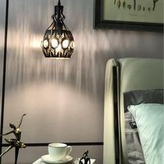 a lamp hanging from the side of a bed next to a table with a cup and saucer on it