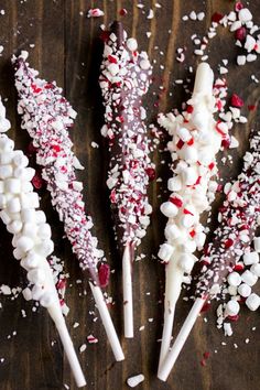 four marshmallow and pepper cane sticks on a wooden table with sprinkles