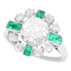 A stunning vintage 2.06 carat diamond and 0.46 carat emerald, 18 karat white gold cocktail ring; part of our diverse emerald estate jewelry collections. This stunning, fine and impressive diamond and emerald ring has been crafted in 18k white gold. The pierced decorated cluster design is ornamented with a feature 1.55Ct Old European round cut diamond, eight claw set in subtle relief to the center of the arrangement. The feature diamond is surrounded by four individually four claw set emerald cut emeralds. The emeralds are separated via a further eight individually six claw set Old European round cut diamonds. The pierced decorated, elevated ring shoulders integrate with the emerald settings and meld seamlessly with the plain ring shank. The ring is hallmarked to the outer surface of the sh Gia Certified Green Diamond Ring In Vintage Style, Vintage Green Diamond Ring In Platinum, Vintage Green Diamond Platinum Ring, Vintage Emerald Ring With Vvs Diamond, Vintage Emerald Ring With Vvs Clarity, White Emerald Ring With Platinum Center Stone, Platinum Emerald Ring With Center Stone In White, Vintage Green Diamond Cluster Ring, White Emerald Platinum Ring With Center Stone