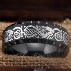 a black and white wedding ring with an intricate design on the inside is sitting on a piece of wood