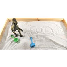 a toy dinosaur plays in the sand with toys like a rake and scoops on it