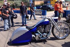 a blue and silver motorcycle parked on the side of a road next to other people