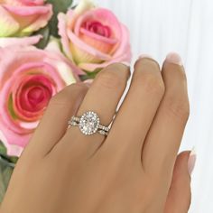 a woman's hand with a diamond ring on it and pink roses in the background