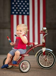 a small child sitting on a tricycle with an american flag in the background