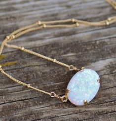 "A stunning necklace made using a lab created opal cabochon. This opal is a lovely shade of white with rainbow fire and flash. The opal is set into a 14K gold filled prong setting and hangs from gold filled satellite style chain. Opal measures 18mm wide (3/4\") or are 14x10mm wide, and is a rounded oval shape. Necklace closes with a gold filled clasp. Please choose desired chain length and opal size at checkout. 18x13mm shown above. Also available in rose gold and silver. Silver will have silver White Oval Adjustable Necklaces, Gold Oval Pink Opal Jewelry, Adjustable Oval White Necklaces, Oval Gold Jewelry With Pink Opal, Oval Pink Opal Gold Jewelry, White Adjustable Oval Necklaces, White Oval Pendant Jewelry With Adjustable Chain, Gold Opal Necklace With Oval Cabochon, Elegant Opal Jewelry With Natural Stones