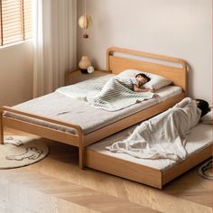 two people laying on beds in a room with wooden floors and white walls, one person is sleeping