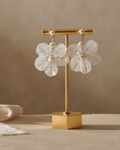 a pair of flower shaped glass earrings on a gold stand next to a white cloth