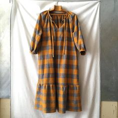 an orange and grey checkered dress hanging on a clothes line with a white wall in the background