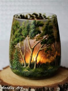 a glass with trees painted on it sitting on top of a piece of tree stump