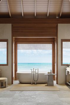 a bathroom with a large bathtub sitting next to two windows overlooking the beach and ocean