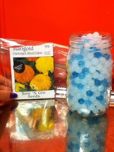 a jar filled with blue and yellow flowers next to a bag of seed seeds on a table