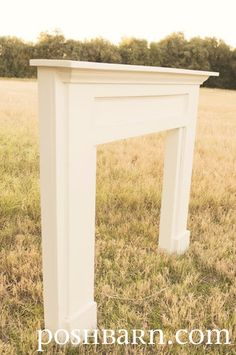 a white fireplace surround in the middle of a grassy field with trees in the background