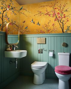 a bathroom with a toilet, sink and mirror next to a wallpapered tree