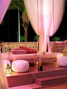 an outdoor seating area is lit up with pink lights and white drapes on the balcony