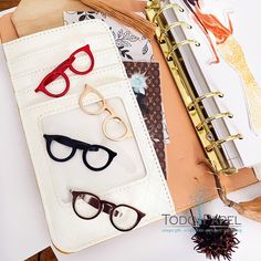 several pairs of glasses sitting on top of a binder next to an open notebook